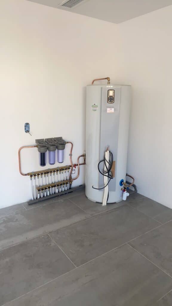 Installation technique moderne avec chauffe-eau Atlantic, trois filtres à eau et un collecteur de distribution en cuivre pour plancher chauffant.